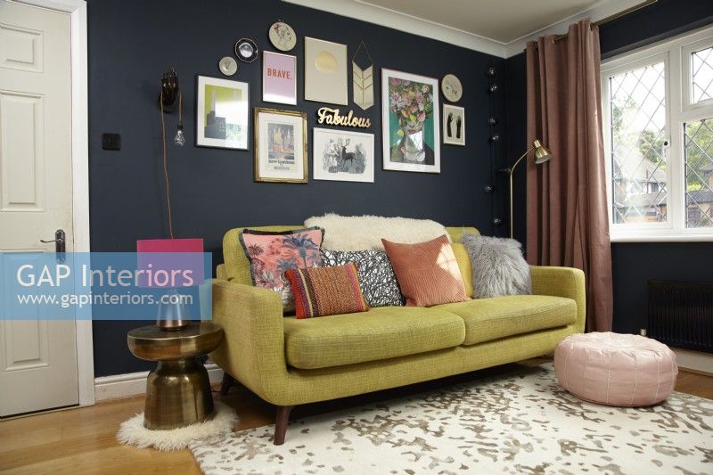 Salon avec un mur de galerie, un canapé vert et un pouf rose.