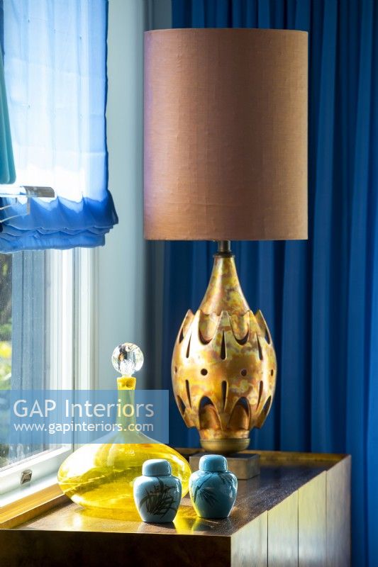 Lampe de couleur bronze sur table avec carafe en verre jaune et pots en céramique bleue.