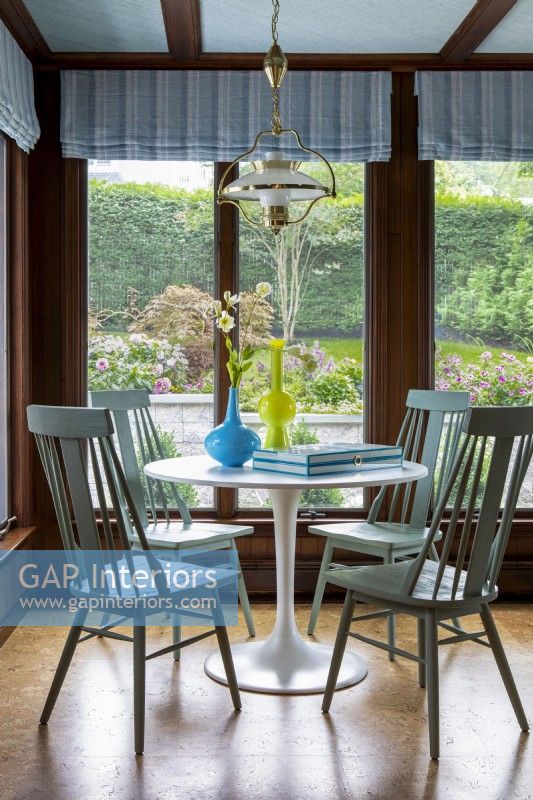 Table à manger ronde sur pied blanc avec chaises en bois et vue sur le jardin.