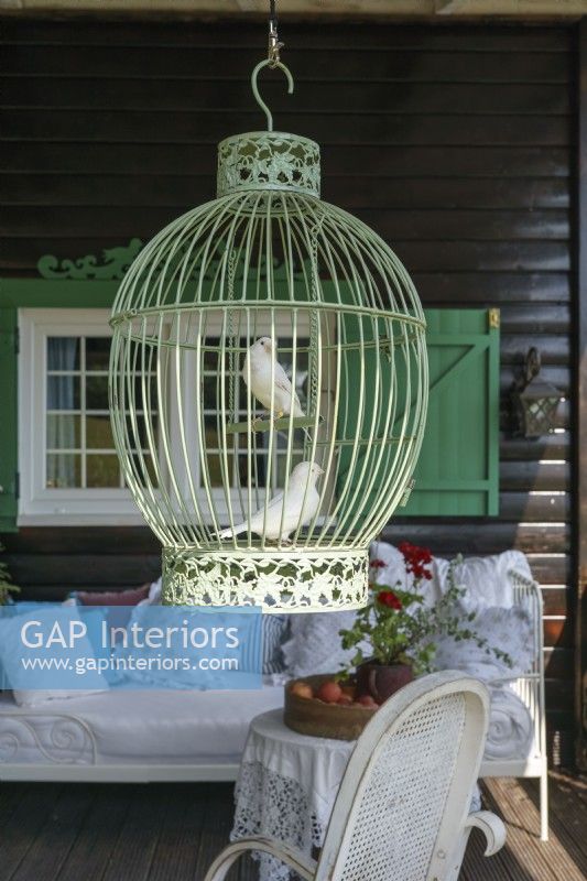 Oiseaux dans une cage verte suspendue devant la maison