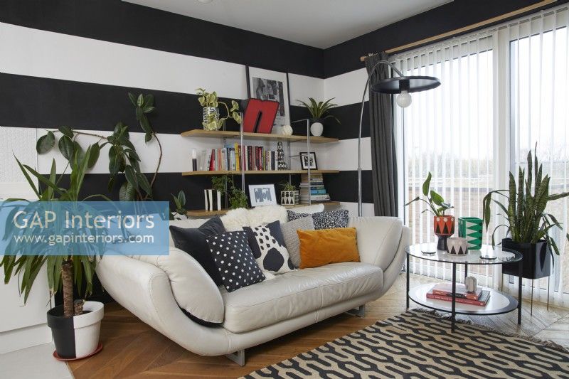 Murs à rayures noires et blanches dans un salon moderne à aire ouverte. Avec un canapé en cuir crème et un tapis à motifs.