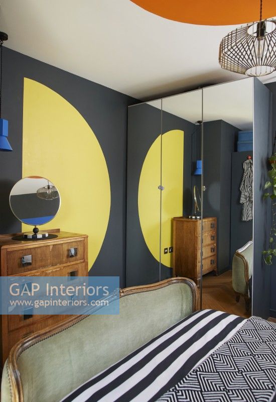 Formes bauhaus peintes audacieuses et colorées dans une chambre contemporaine. Montrant un demi-cercle jaune, une commode vintage et une armoire à glace.