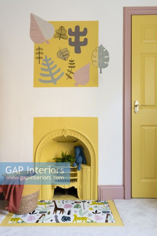 Cheminée victorienne peinte en jaune dans une chambre d'enfant avec foyer recouvert de vinyle et d'art mural au pochoir