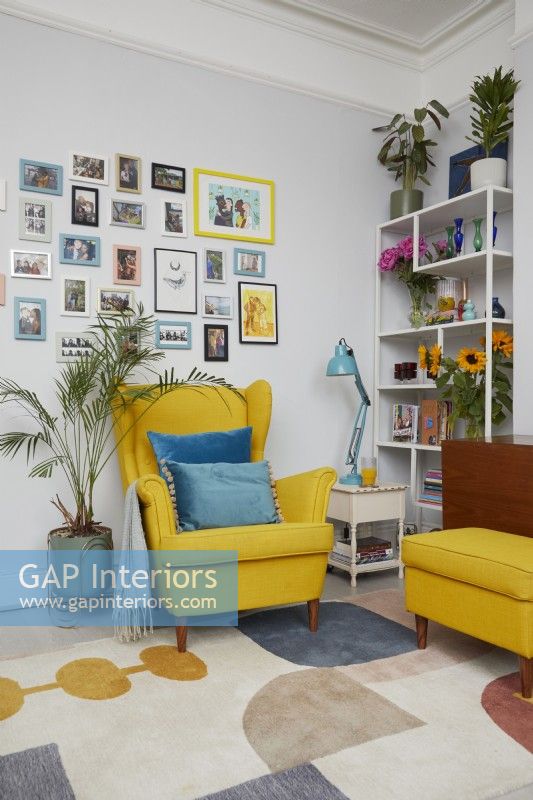 Coin salon montrant un fauteuil et un repose-pieds jaunes de style milieu du siècle avec un mur de galerie, une étagère et des plantes.