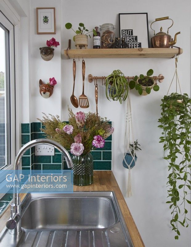 Détail d'une cuisine contemporaine avec évier, carreaux de métro verts et étagères ouvertes avec des plantes.