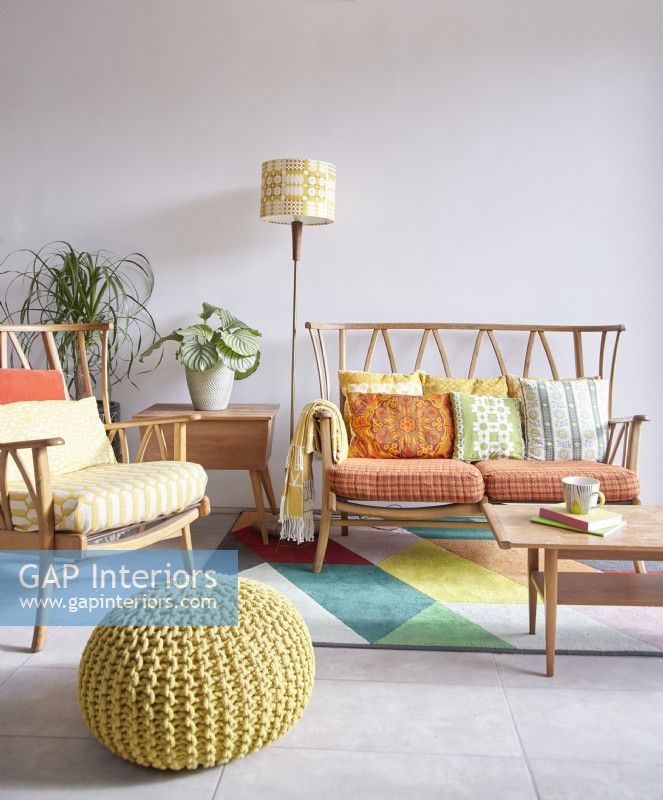 Espace de vie décloisonné montrant un coin salon avec des meubles vintage Ercol avec des coussins rétro, un pouf et un tapis.