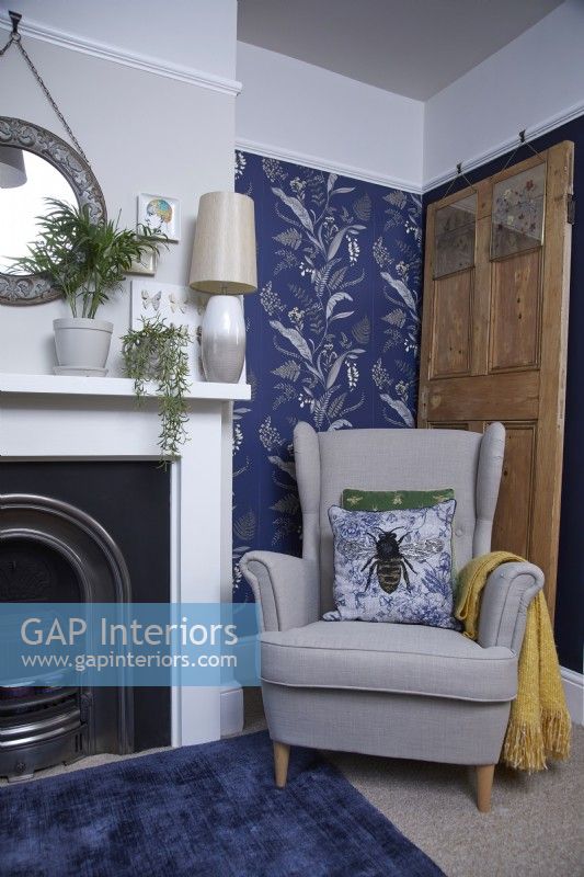Salon avec cheminée, fauteuil cosy et papier peint à motifs bleus.