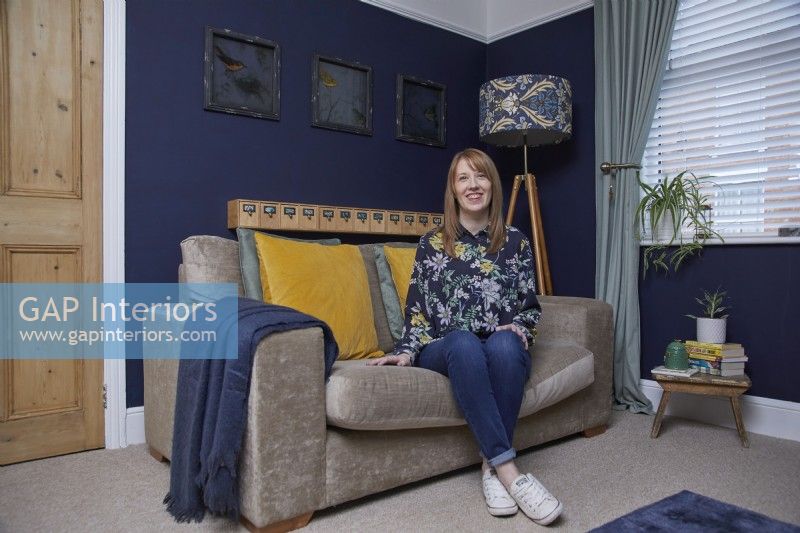 Salon avec des murs peints en bleu foncé, un canapé en velours gris et un lampadaire à motifs.