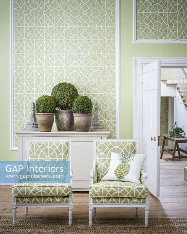 Deux chaises à motifs verts devant un mur de panneaux recouverts de papier peint