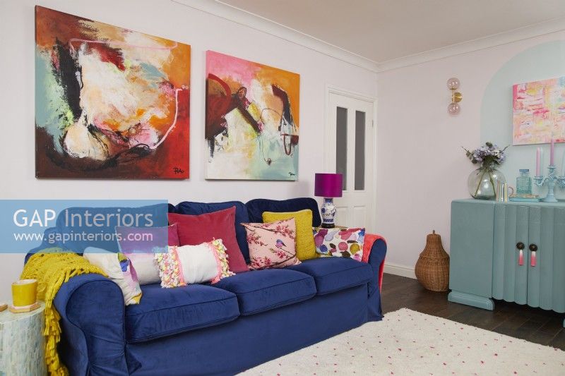 Salon coloré avec un canapé en velours bleu foncé, de grands tableaux et une armoire turquoise recyclée.