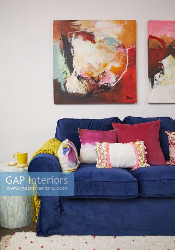 Détail coloré du salon avec un canapé en velours bleu foncé, des coussins colorés et de grands tableaux abstraits.