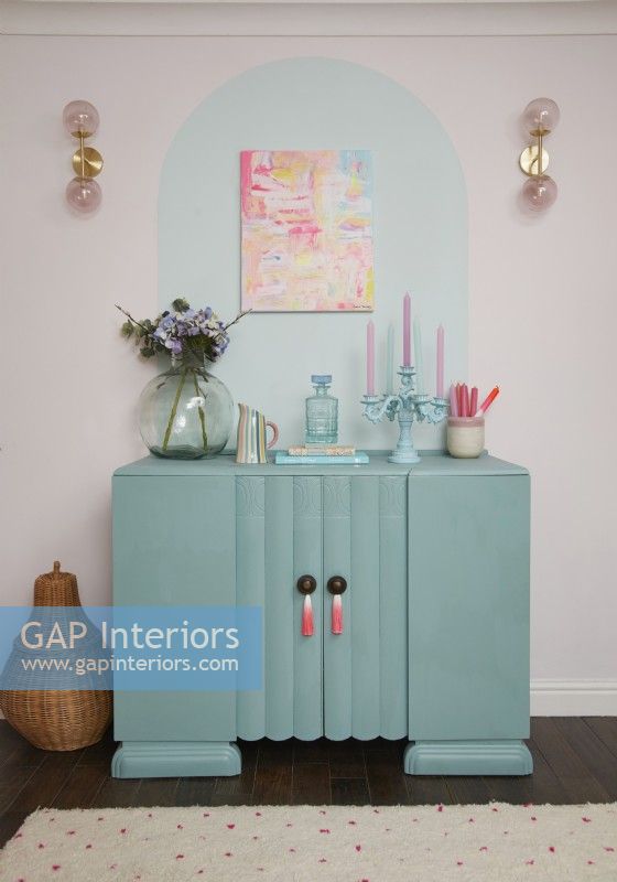 Salon montrant une armoire turquoise recyclée avec des détails muraux peints et une peinture abstraite.
