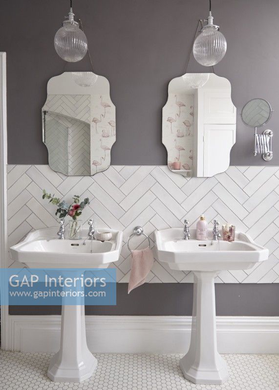 Salle de bain avec double vasque, carrelage blanc à chevrons et miroirs de style vintage.