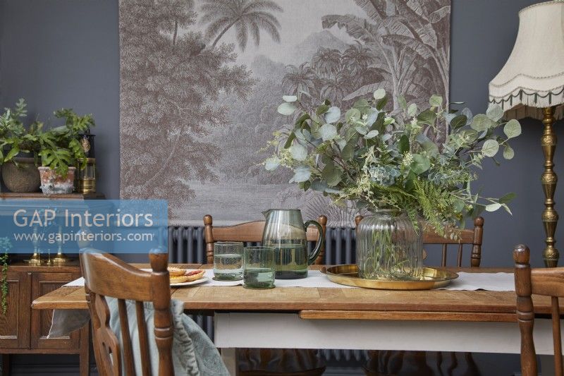 Détail de la salle à manger montrant une table avec de la verrerie, des meubles en bois vintage et des œuvres d'art botaniques.