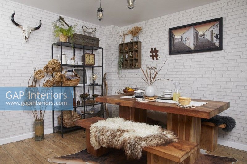 Coin repas avec une table en bois, des étagères de style industriel et un papier peint en briques blanches.