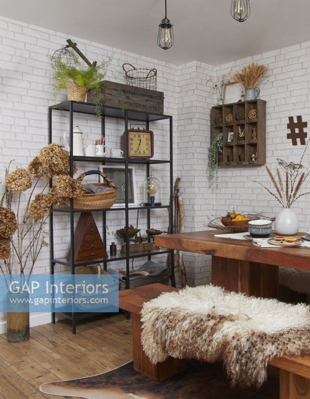 Coin repas avec une table en bois, des étagères de style industriel et un papier peint en briques blanches.