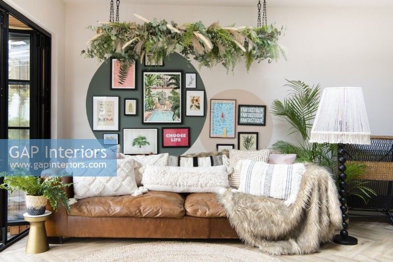 Canapé en cuir marron devant un mur de galerie avec de fausses plantes suspendues