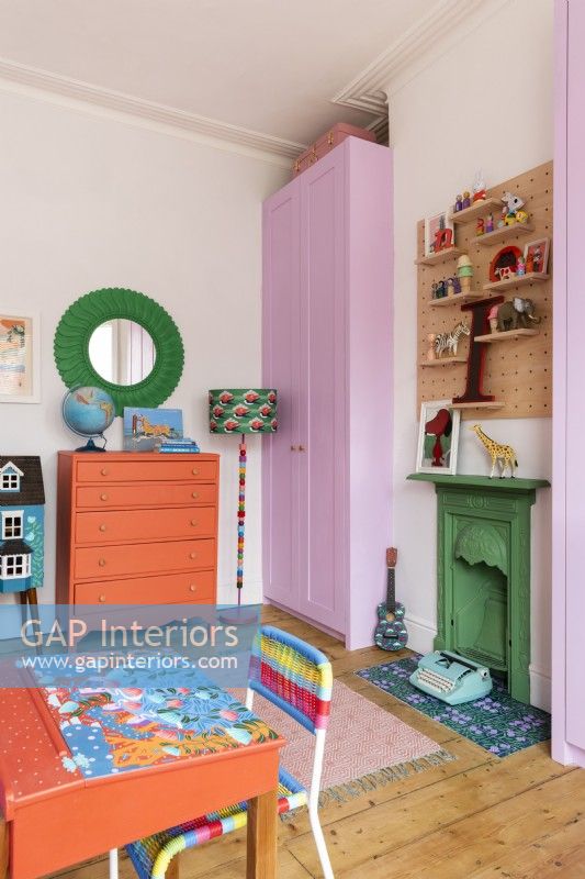 Armoire encastrée rose et cheminée verte peinte dans une chambre d'enfant avec bureau d'école peint à la main