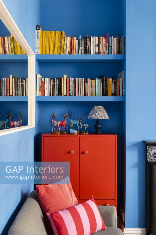 Armoire peinte en rouge recyclée dans un salon bleu avec une étagère à livres au-dessus