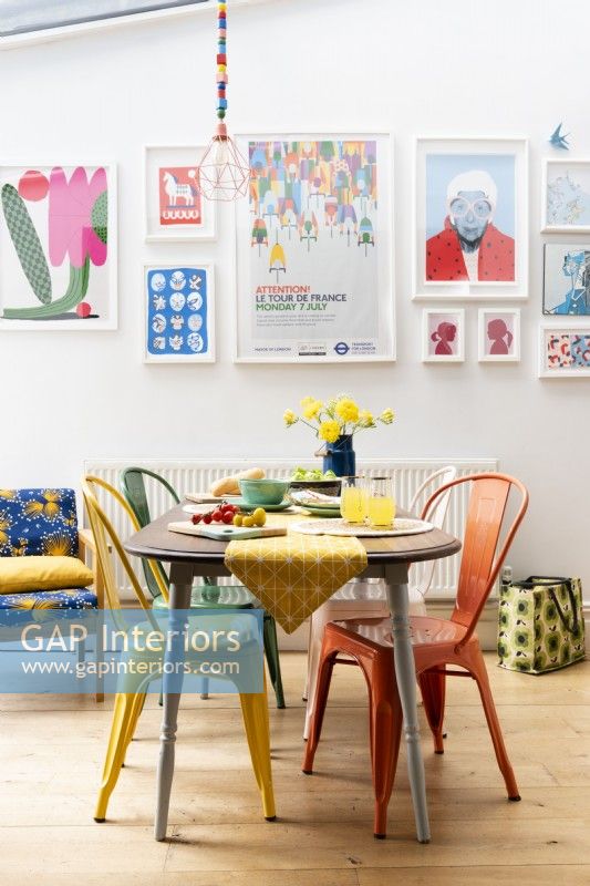 Table à manger récupérée avec différentes chaises en métal colorées devant un affichage mural coloré d'art encadré