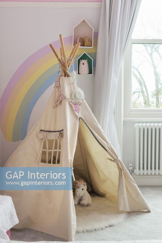 Jouez à la tente tipi dans la chambre des enfants avec un arc-en-ciel peint sur le mur