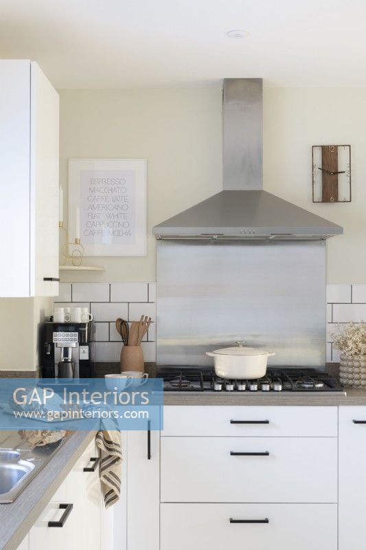 Crédence en acier inoxydable et hotte aspirante derrière une cuisinière à gaz dans une cuisine blanche moderne