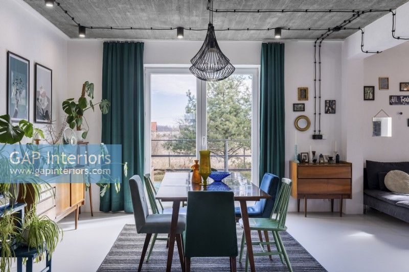 Salle à manger rétro avec grande table, mélange de chaises, plantes et fenêtre en arrière-plan