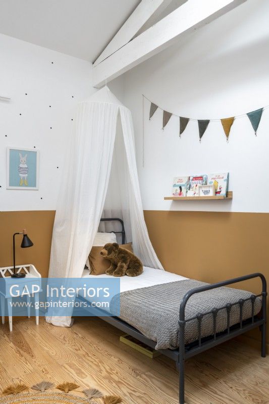 Auvent au-dessus d'un lit simple dans une chambre d'enfant avec un mur peint divisé
