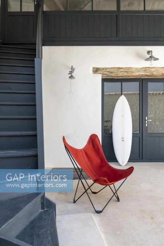 Designer chair and surfboard at bottom of stairs in modern hallway