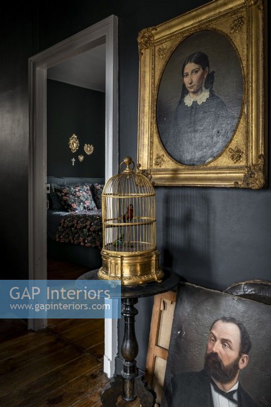Portraits classiques et cage à oiseaux dorée contre un mur peint en noir