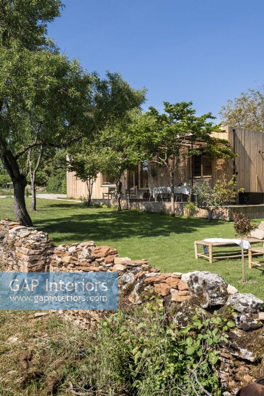 Mur de pierre rustique menant à un jardin de campagne avec des espaces de vie extérieurs