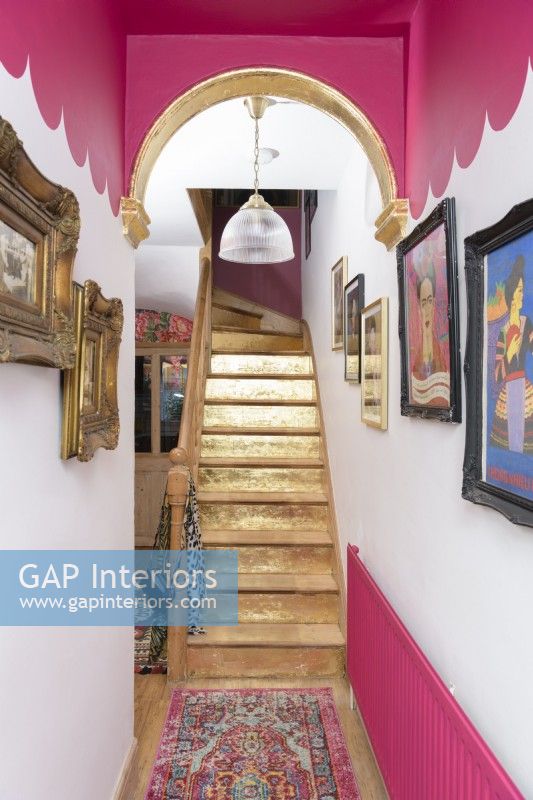 Un escalier peint en or dans un couloir peint en rose et blanc festonné