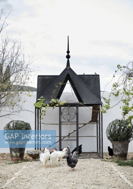 Poulailler noir orné dans une cour blanche avec des poules