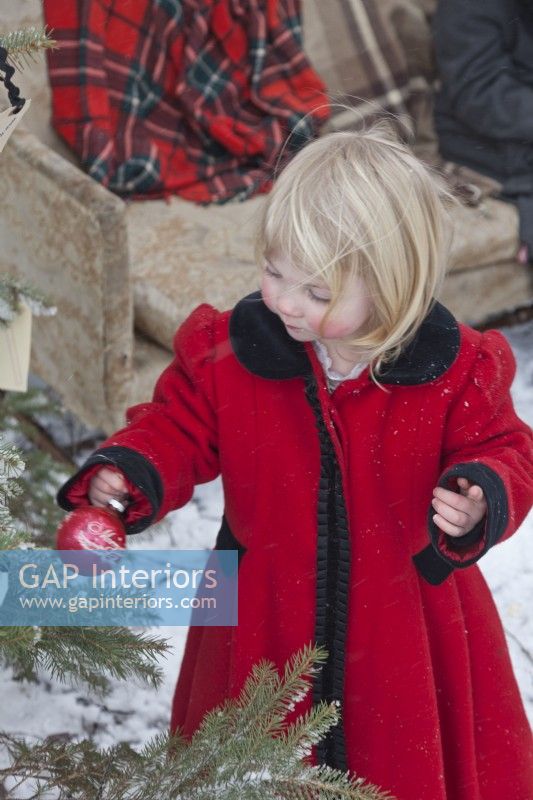 Petites filles portant un manteau vintage rouge et décorant un arbre de Noël en plein air dans la neige