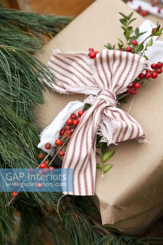 Gros plan sur un cadeau de Noël enveloppé dans du papier brun décoré de ruban, de verdure et de baies