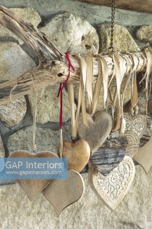 Collection de coeurs du monde entier dans des matériaux et des tailles variés suspendus au bois flotté sur la cheminée du salon.
