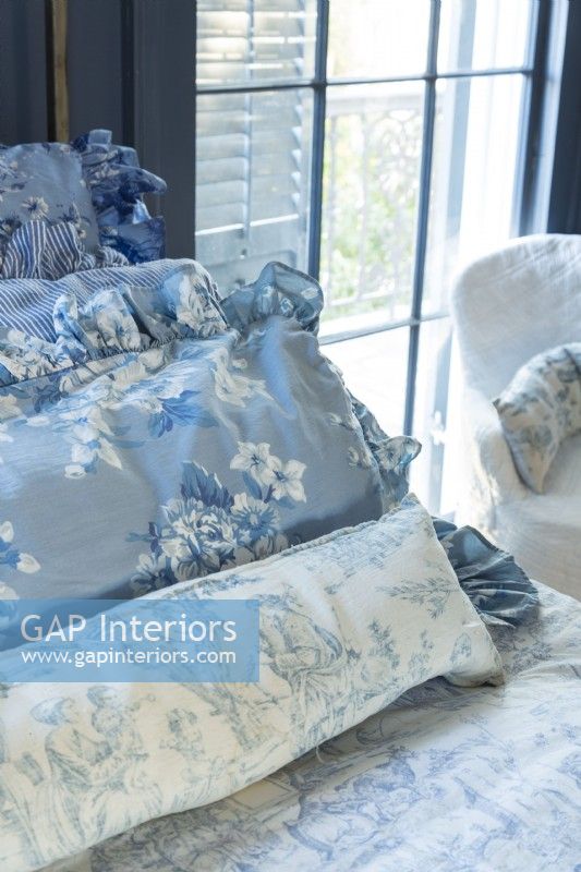 Renee garde le thème bleu et blanc français de la chambre à coucher fluide avec des oreillers arborant des variations de teintes et des motifs floraux et pastoraux.