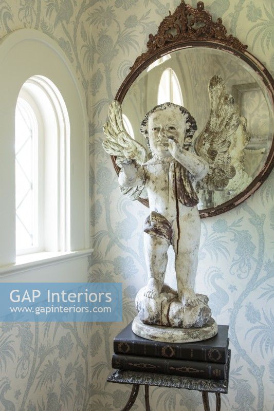Le foyer abrite un ancien chérubin français, un miroir vintage et une table en métal. Le délicat papier peint bleu et blanc annonce la palette de couleurs de l'intérieur de la maison.