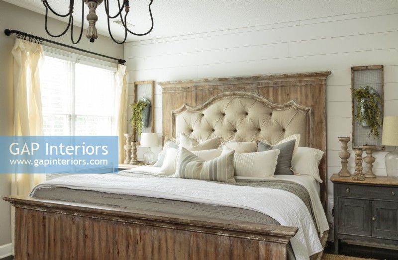 Un mur à déclin et une variété de bois vieillis créent un sens de l'histoire dans la chambre du couple. Le lit king-size est doté d'un cadre de tête de lit en détresse avec un rembourrage capitonné superposé à un panneau de cheminée en bois blanchi à la chaux rustique.