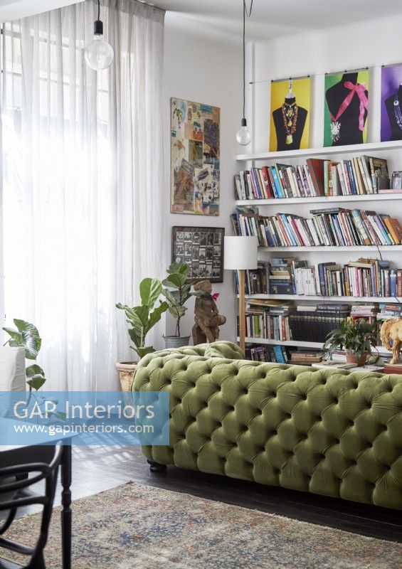 Canapé clouté vert dans le salon avec de grandes étagères et des œuvres d'art