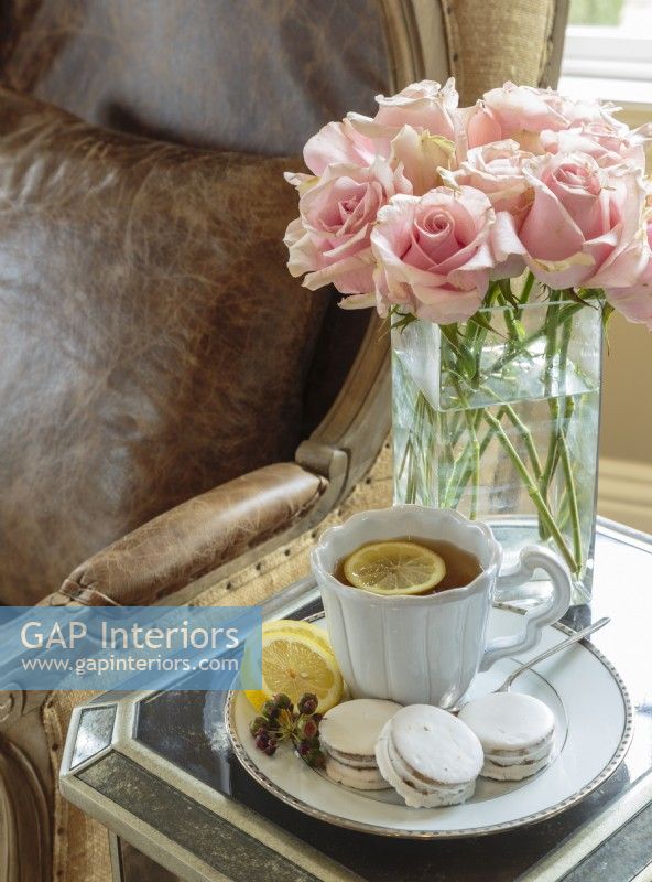 Du thé, des biscuits et des roses posés sur une table miroir sont parfaitement à l'aise à côté d'un confortable fauteuil en cuir.