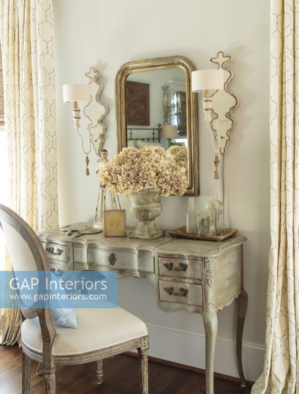Habilement refinie par Anita, une vanité sinueuse partage le devant de la scène avec un miroir Louis Philippe et des appliques murales en bois soulignées de peinture dorée.