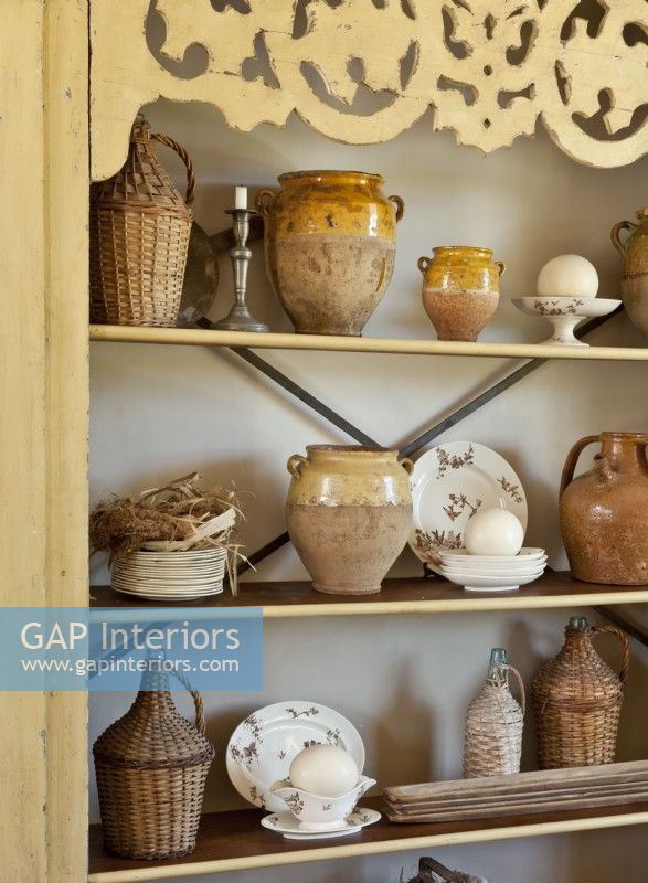 L'armoire antique contient un assortiment de cruches enveloppées d'osier, de pots d'huile d'olive et de plats vintage.