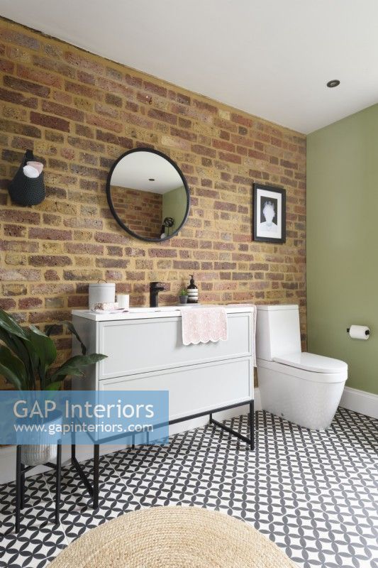 Meuble lavabo blanc avec tiroirs et toilettes contre un mur en briques apparentes dans une salle de bains moderne