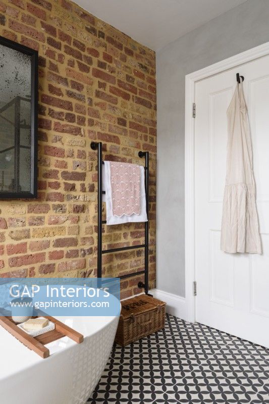 Un porte-serviettes noir dans le coin d'une salle de bain avec des briques apparentes et une porte blanche contre un mur de ciment gris lisse avec un sol carrelé à motifs monochromes