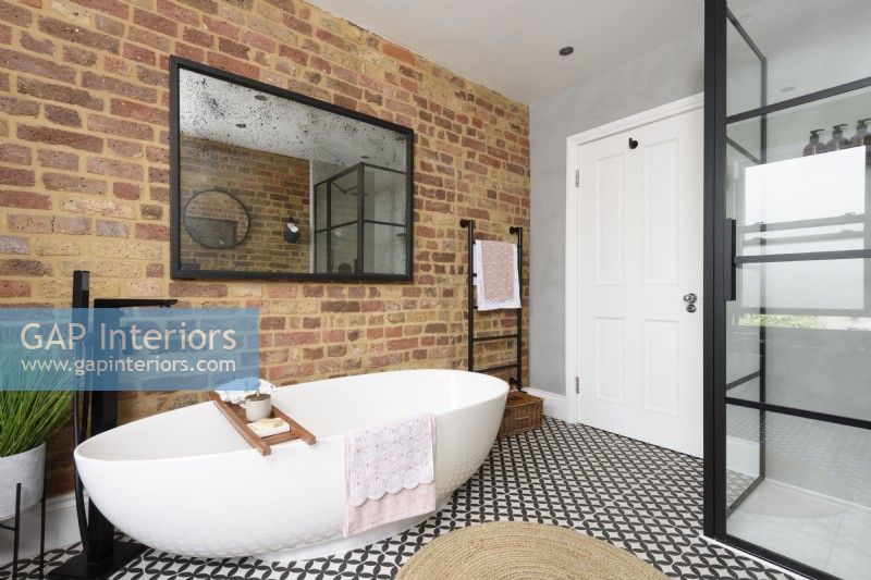 Salle de bains moderne monochrome avec une cabine de douche crittall et une baignoire en céramique en forme de coquille d'oeuf contre un mur de briques apparentes