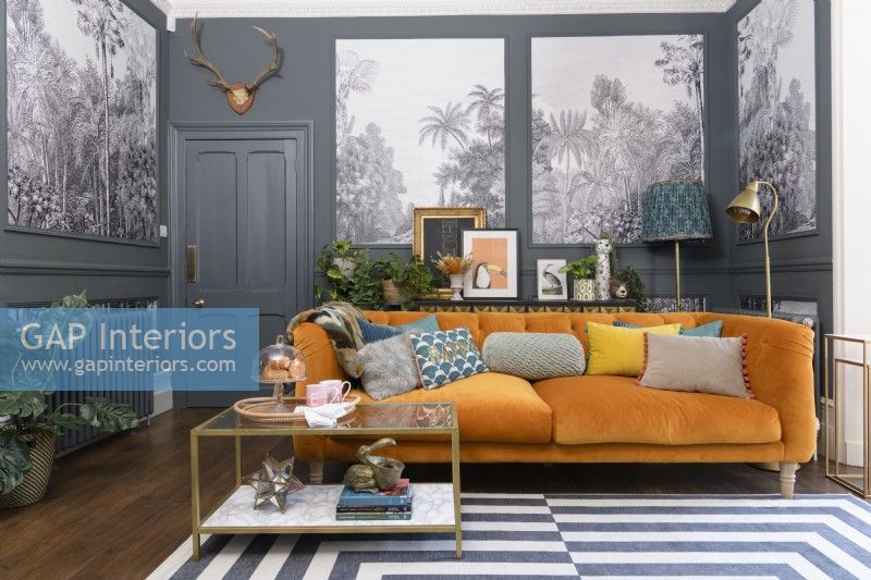 Canapé en velours orange dans un salon gris avec des panneaux remplis de papier peint monochrome à motifs d'arbres tropicaux