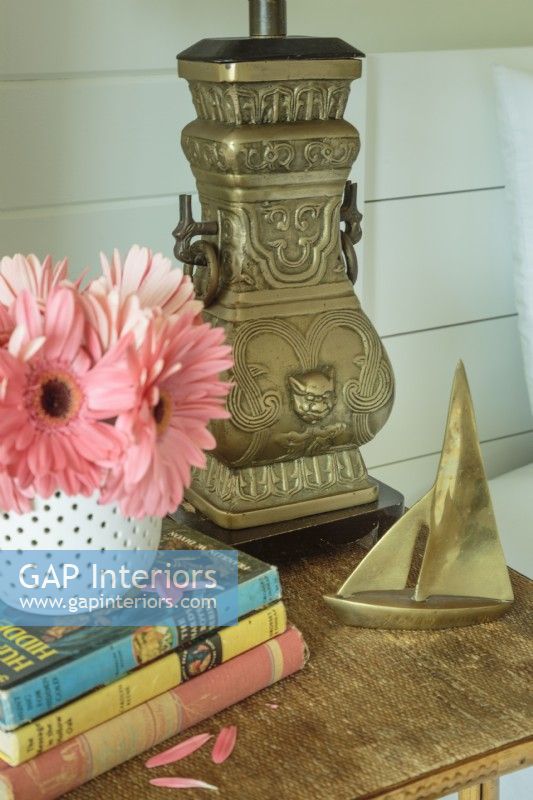 Une lampe en métal en forme d'urne et un petit voilier en laiton ornent une table de chevet.