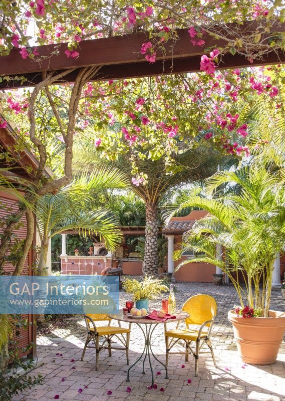 Une table de bistro nichée sous des vignes de bougainvilliers et des palmiers évoque une cour toscane en plein air