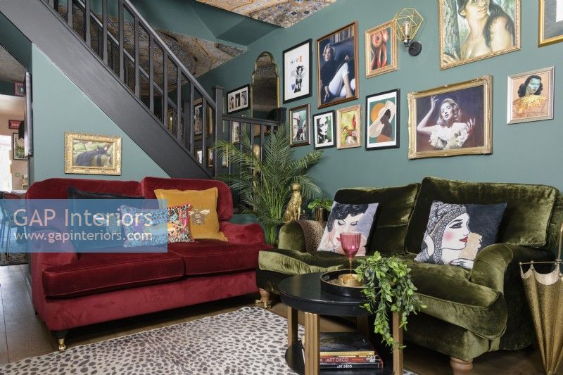 Salon vert ouvert avec canapés en velours rouge et vert devant un escalier ouvert et un mur d'exposition d'art de style salon